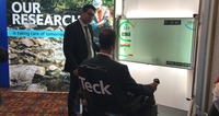 Demonstration of research technology with interactive display at an exhibition, two men present.